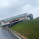 Tovornjak s priklopnikom zapeljal z vozišča na brežino in obtičal z dvignjenimi kolesi
